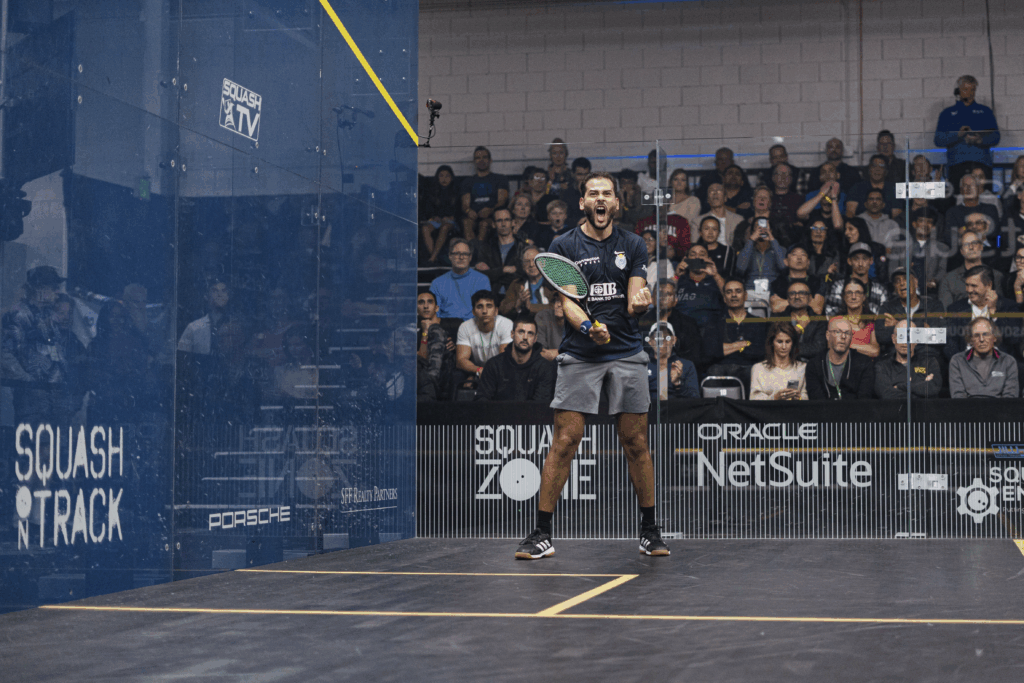 Squash player in action on a squash court with spectators in the background